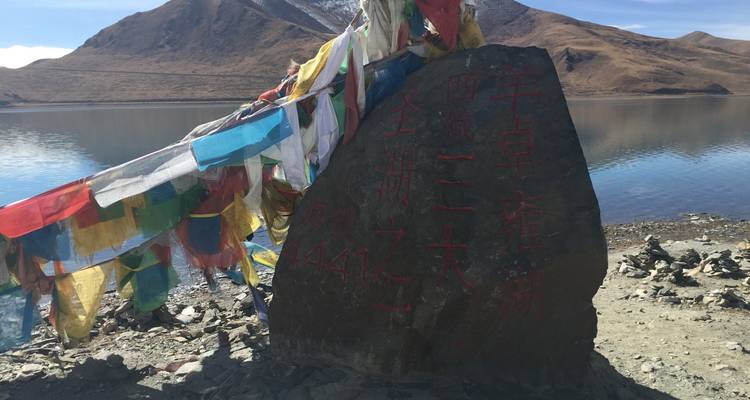 Roca con banderas coloridas junto a un lago y montañas.