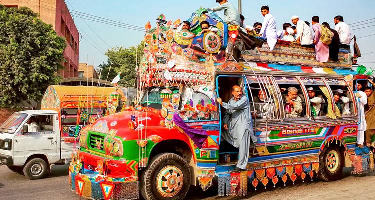 Autobús tradicional colorido cargado de pasajeros en una calle concurrida.