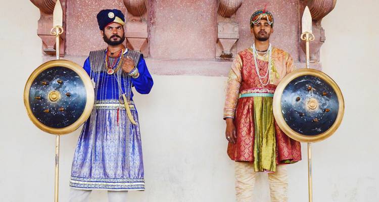 Dos hombres vestidos con trajes tradicionales de guardia están de pie con escudos y lanzas.