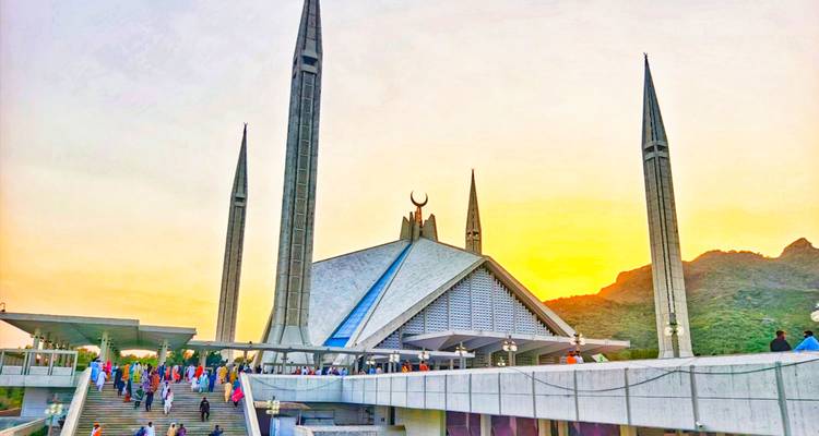 Una mezquita con minaretes altos vista al atardecer con personas caminando alrededor.