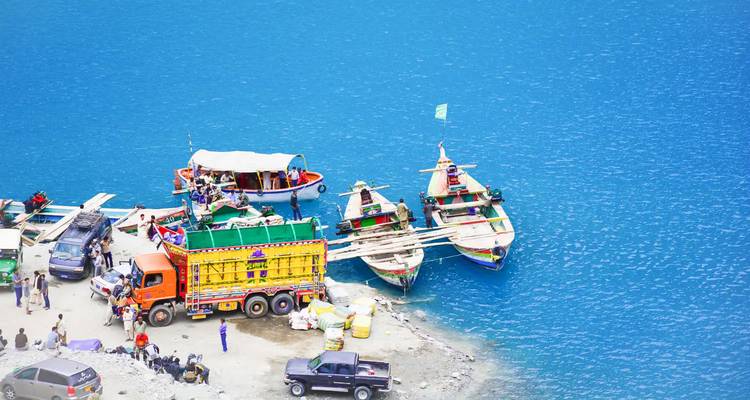 Botes atracados en la orilla de un lago azul brillante junto a camiones coloridos.