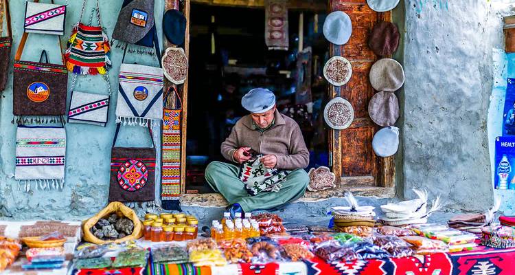 Hombre elaborando artesanías en un mercado tradicional con productos tejidos coloridos.