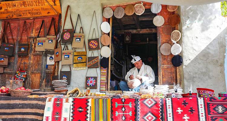 Hombre vendiendo artesanías coloridas y alfombras en un mercado tradicional.