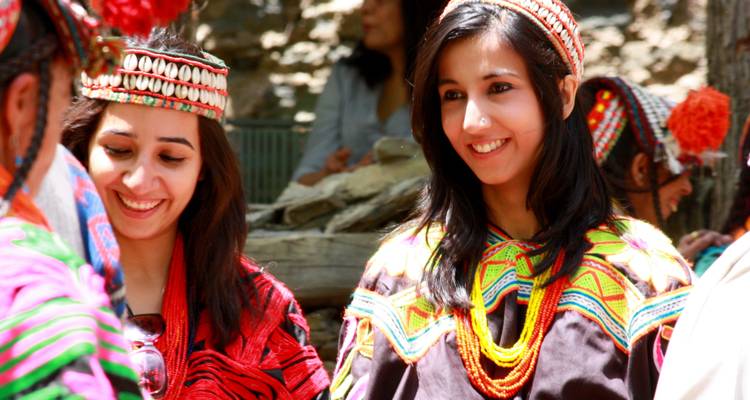 Deux femmes en robes traditionnelles colorées souriant à l'extérieur.