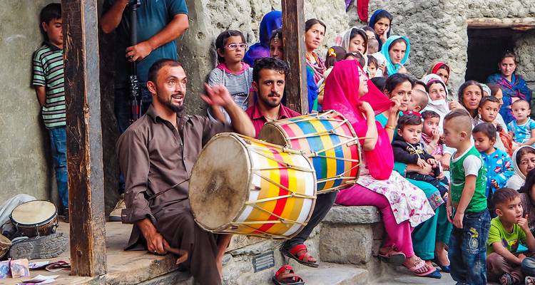 A group of people with traditional musical instruments, gathering outside a rustic building.