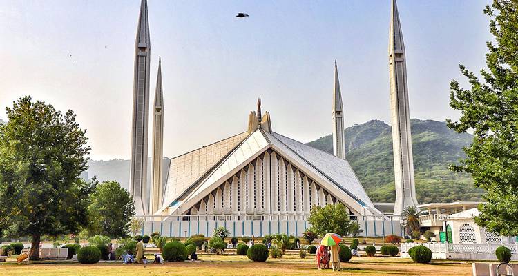 A modern mosque with tall minarets and green gardens.