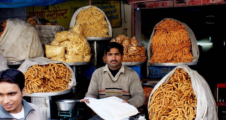 Verkoper die stapels gefrituurde snacks verkoopt op een markt.