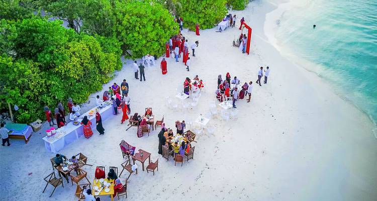 Dîner de plage avec tables et invités sur le sable.