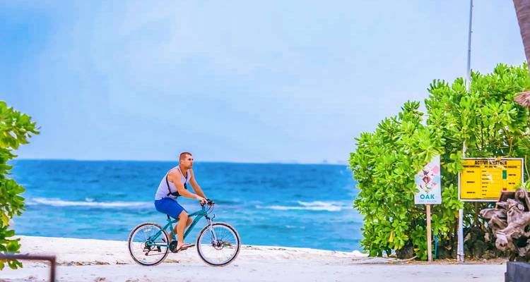 Man cycling on a path by the beach with blue ocean in the background.