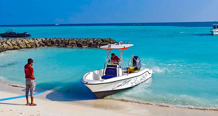 Small speedboat approaching a sandy beach next to clear blue waters.