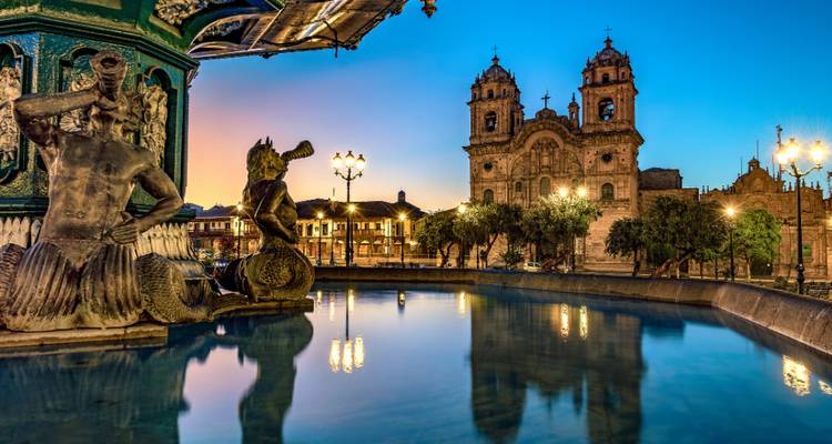 Avondlichten weerspiegelen in een fontein op Cusco's Plaza de Armas met de kathedraal die gloeit in de schemering.