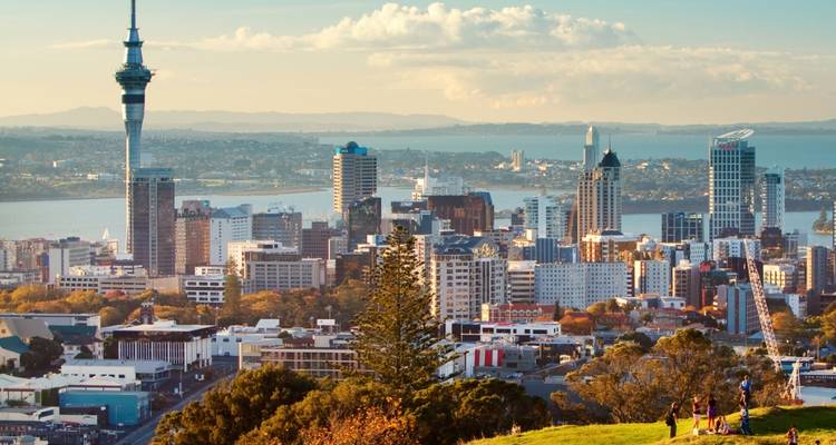 Panoramischer Blick auf die Skyline von Auckland mit dem Sky Tower, der sich über dem Hafen und den entfernten Hügeln erhebt.