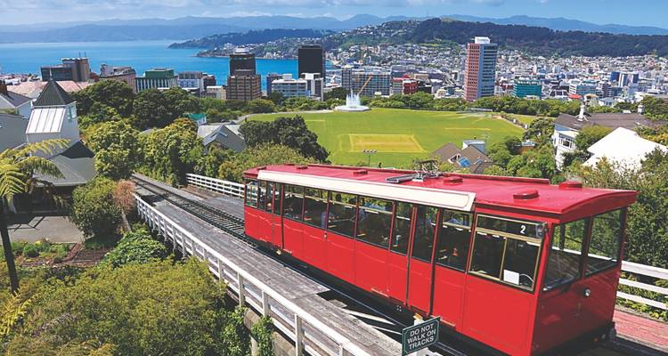 Ikonische rote Wellington-Zahnradbahn erklimmt Hügelhang mit Panoramablick auf den Hafen.
