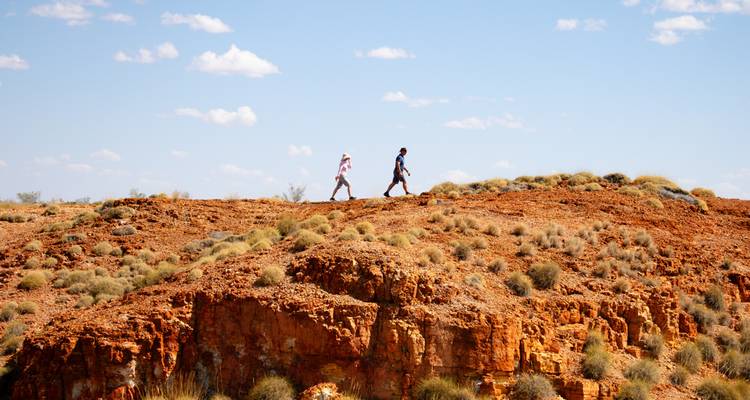 Two people hiking on a rocky ridge under a blue sky.