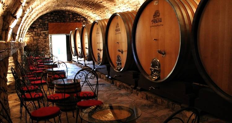 Interior of a wine cellar with large wooden barrels and empty tables and chairs.