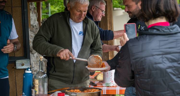 Local cook ladles hearty food onto a plate for hungry travellers at an outdoor table.