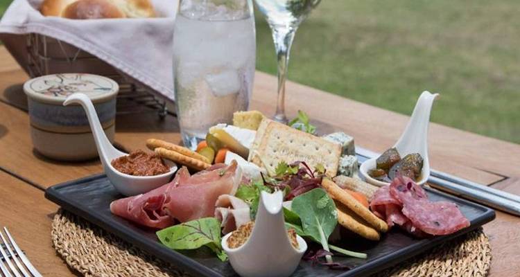 Gourmet meal with meats, cheese, and drinks on a patio.