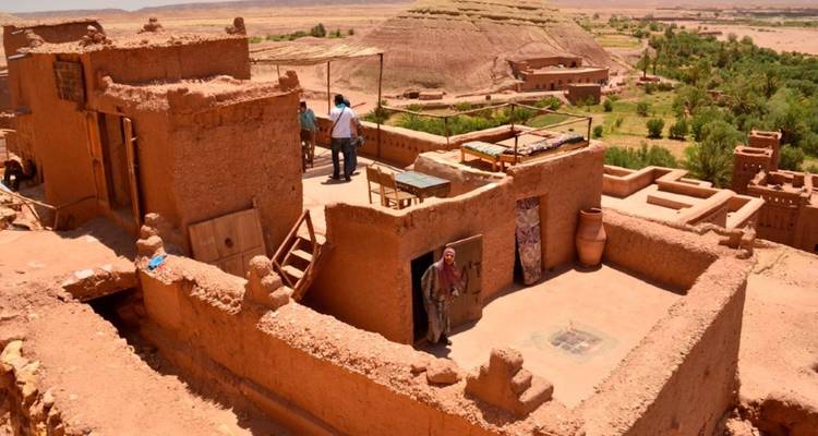 People on a rooftop terrace of a clay building with desert views.