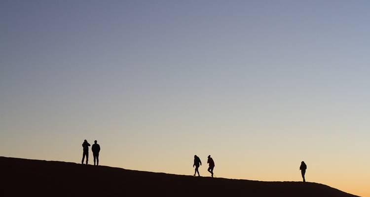 Silhouetted figures walking on a ridge at sunset.