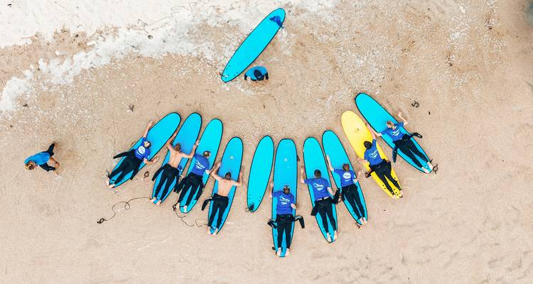 Aerial view of a group of surfers with surfboards on a beach.