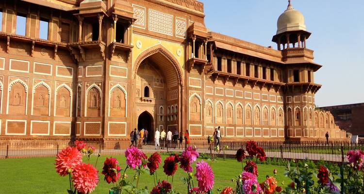 Groot rood zandstenen gebouw met ingewikkelde beeldhouwwerk, bloemen op de voorgrond.