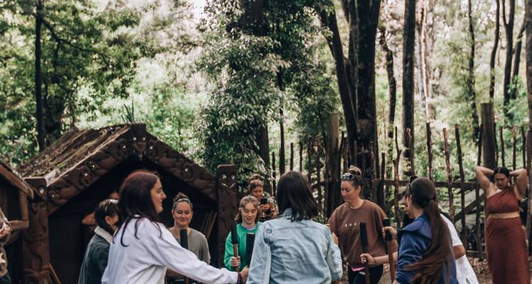 Gruppe von Reisenden nimmt an einer Kulturveranstaltung in einem üppigen Maori-Walddorf teil