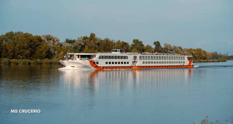 Wit en oranje riviercruiseschip vaart op een kalme rivier omzoomd met bomen.