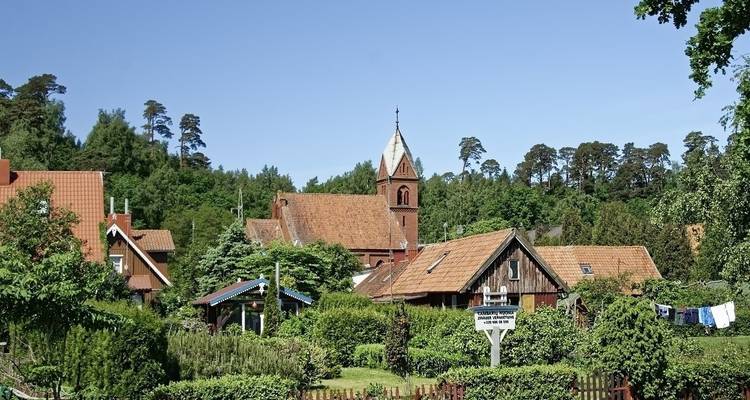 Rural village with wooden houses and a church in a wooded area.