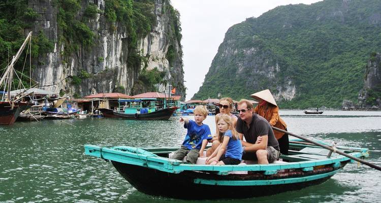 Una familia en un barco rodeada por acantilados de piedra caliza y embarcaciones tradicionales.