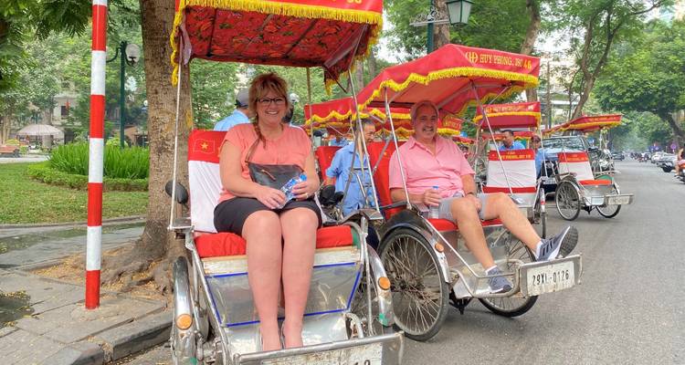 Turistas sentados en rickshaws en una calle arbolada.
