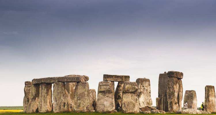 Les menhirs préhistoriques de Stonehenge se dressent contre un ciel gris dramatique avec des champs s'étendant au-delà.