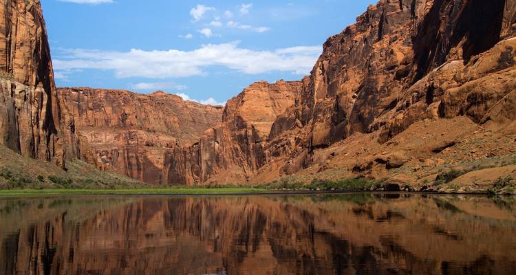 Reflections of canyon walls and clear sky on a calm river.