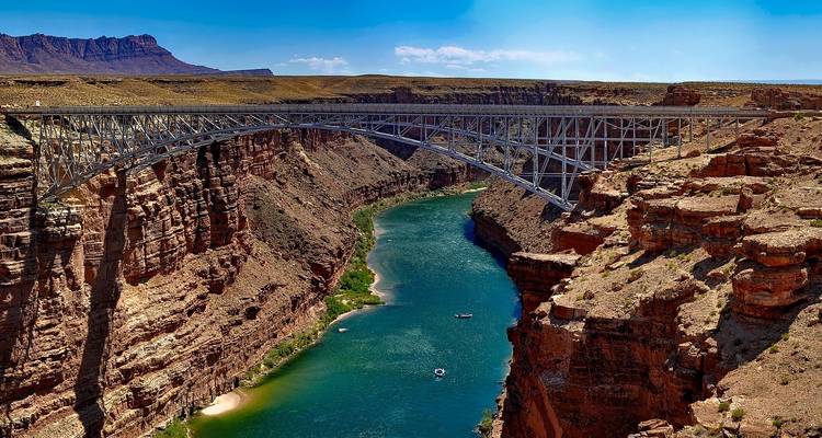 Bridge spanning over a deep canyon with clear blue river below.
