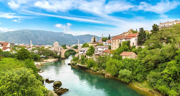 Schöne Aussicht auf einen Fluss mit einer ikonischen Steinbrücke vor einer Kulisse aus Bergen und historischen Gebäuden.