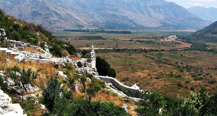Weiter Blick über ein Tal mit Steinruinen und Bergen in der Ferne.