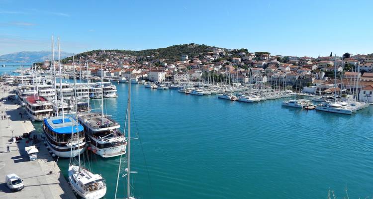 Rijen jachten liggen in een levendige blauwe haven tegenover het heuvelachtige, witgekalkte stadje Trogir.