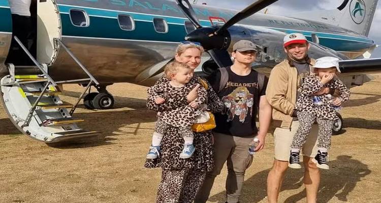 A family standing in front of a small plane on a savannah airstrip.