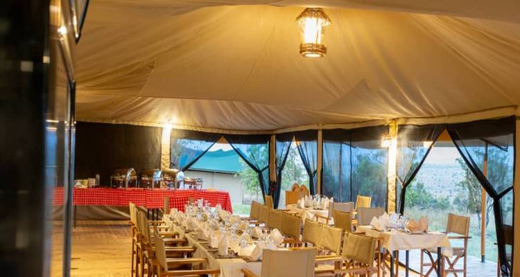 Dining setup in a safari tent with tables set for a meal.