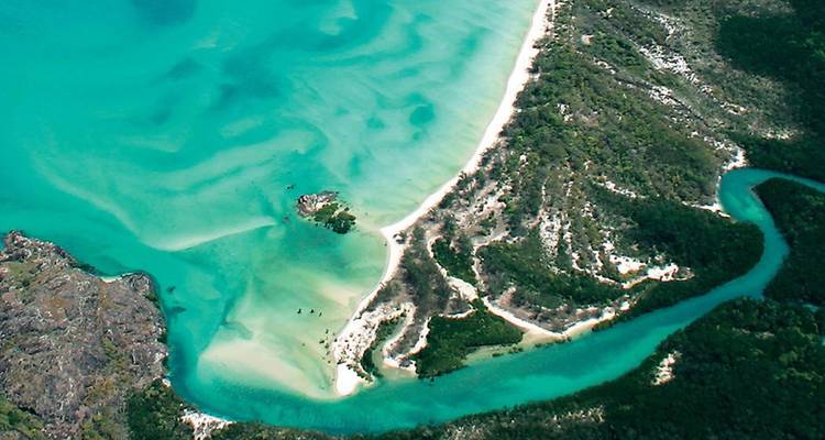Luchtfoto van een turquoise baai, wit zand en een kronkelende rivier in tropische wildernis.