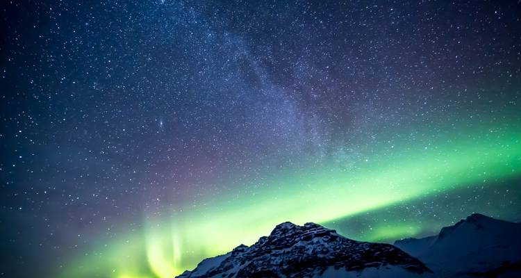 Brilliant green aurora borealis dances above a snow-capped mountain under a starry sky.