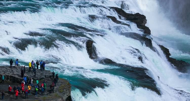 Tourists gather on rocky ledges beside the powerful tiered cascades of Gullfoss waterfall.