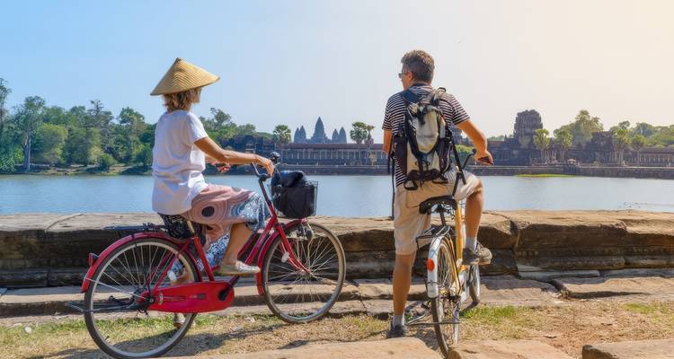 Deux cyclistes observant le complexe du temple d'Angkor Vat à distance.