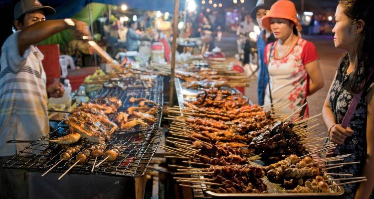 Un marché nocturne animé avec des gens qui achètent de la nourriture de rue grillée.