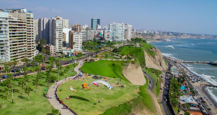 Paragliders soar above green cliffs and modern seaside skyline along the Pacific coast.