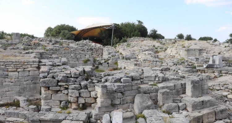 Ruines anciennes avec formations rocheuses et arbres sous un ciel dégagé.