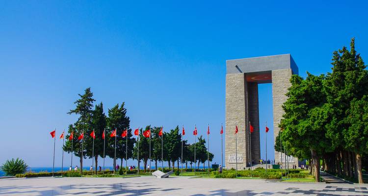 Site commémoratif avec des drapeaux et des structures de style moderne contre un ciel bleu.