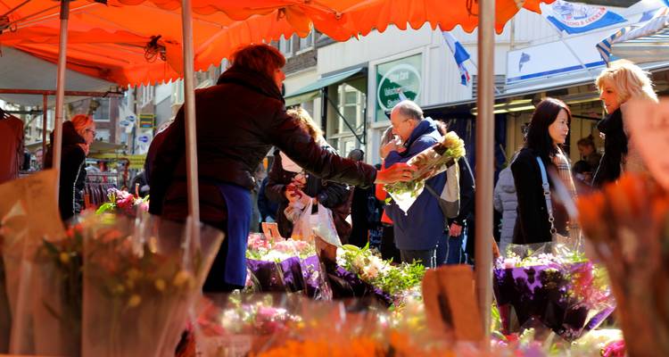 Marché animé avec des étals de fleurs, des gens qui flânent.