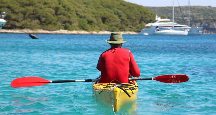 Hombre navegando en kayak en aguas azules cristalinas con yates al fondo.