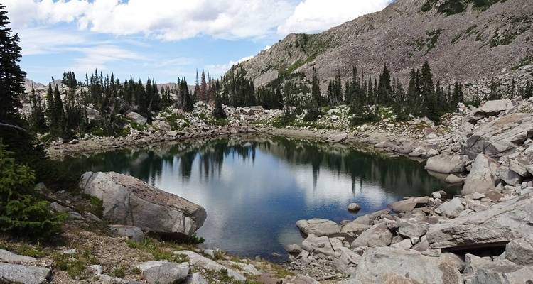 Small alpine lake surrounded by rocks and conifer trees.