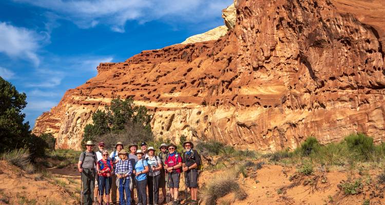 Group of hikers in front of red rock cliffs and clear blue sky.